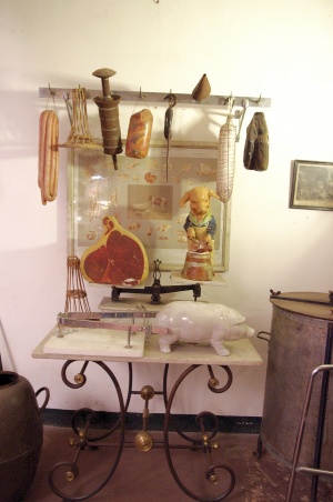 Table de boucher pour la présentation des viandes, supportant des objets de boucherie et enseignes et surmontée d'un croc où pendent des viandes factices.